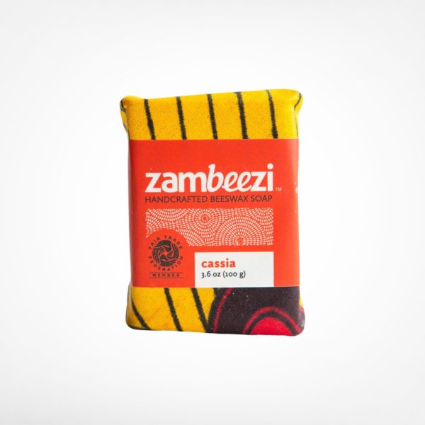 Rectangular bar of soap wrapped in vibrant cloth with a geometric design. Label reads: Zambeezi, handcrafted beeswaz soap: Cassia, 3.6 oz (100g)